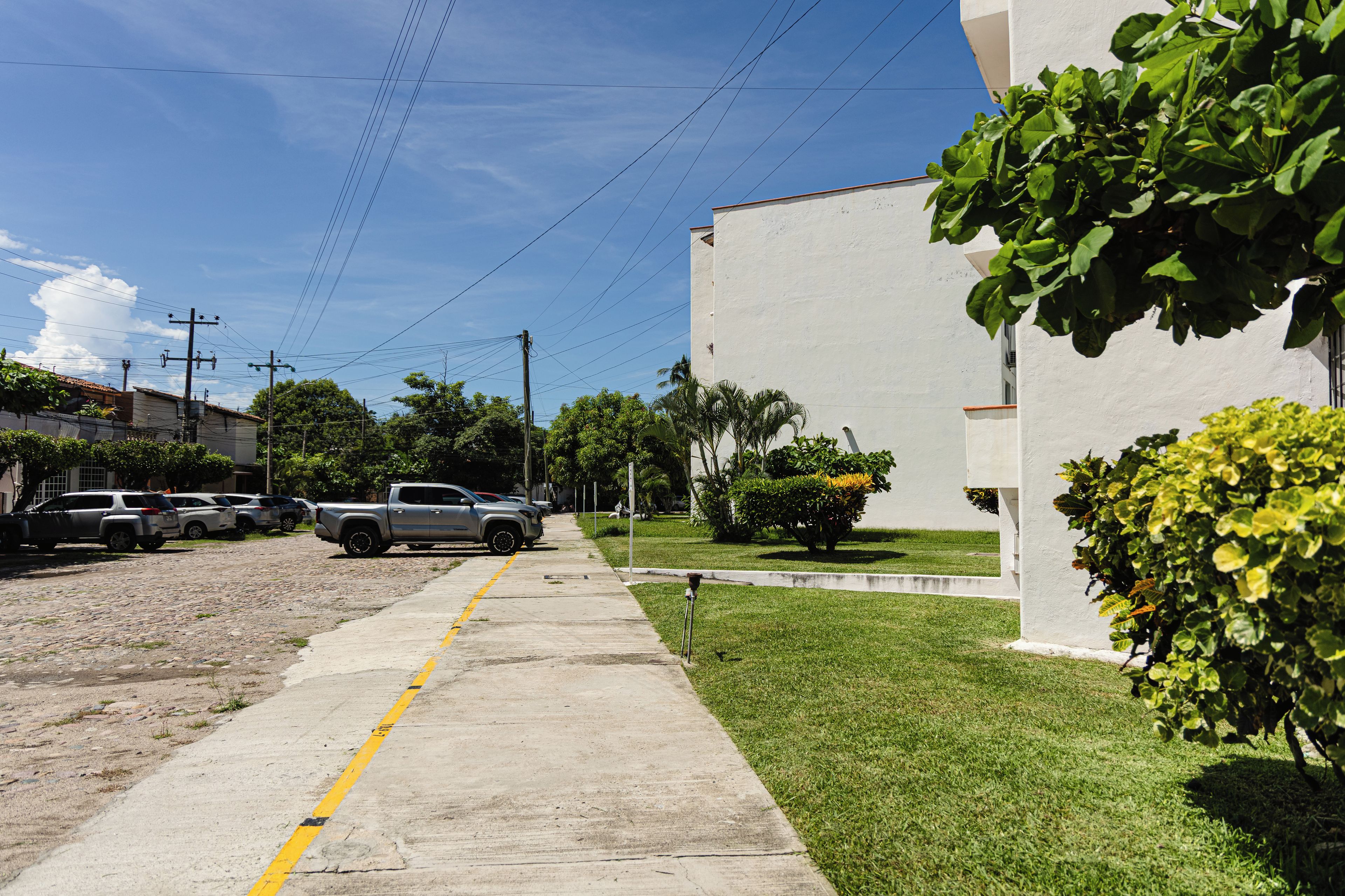A street with parked cars, a sidewalk, and a building with a white exterior.