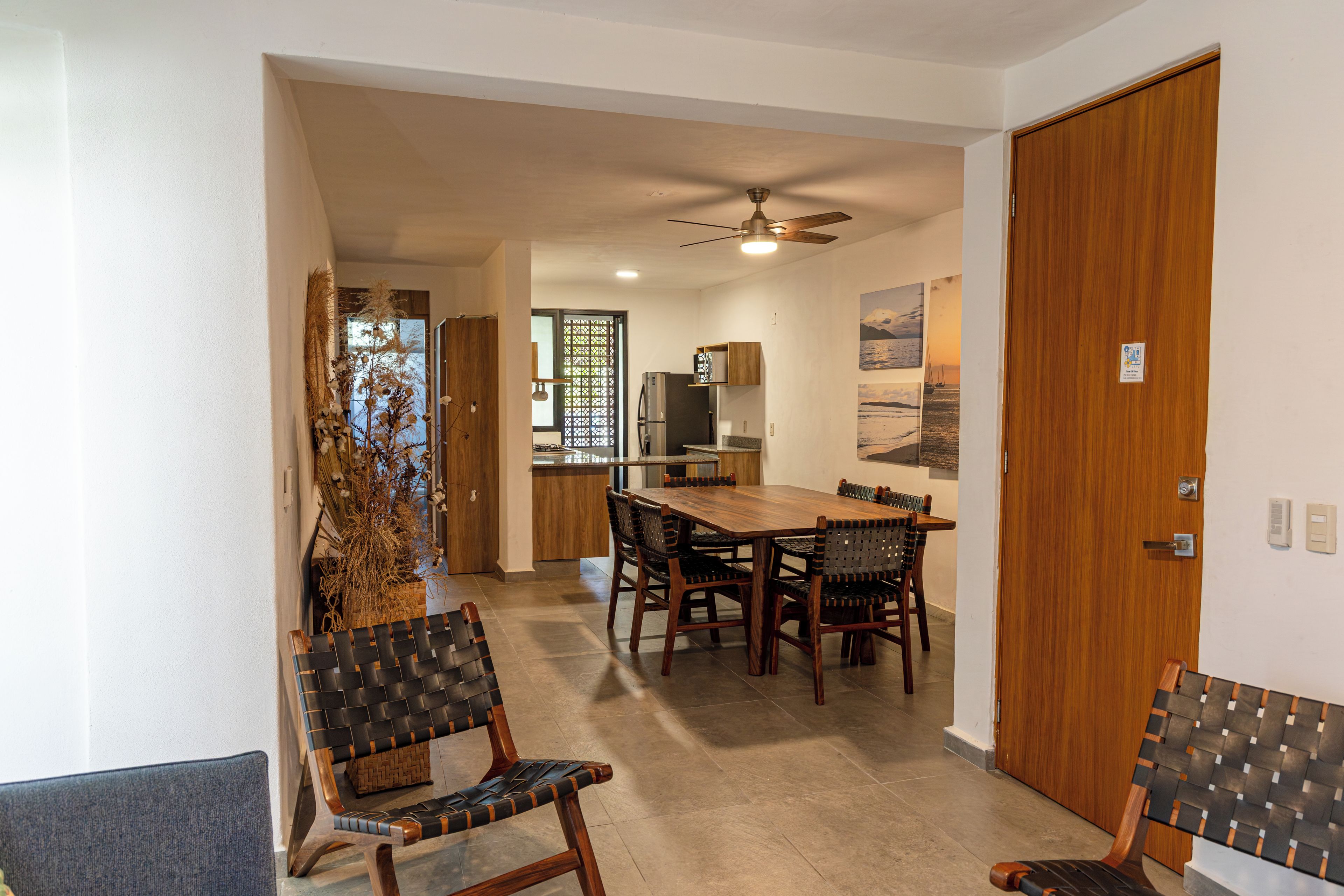 A dining area with a wooden table and chairs, a ceiling fan, and a view of the kitchen through a glass door.
