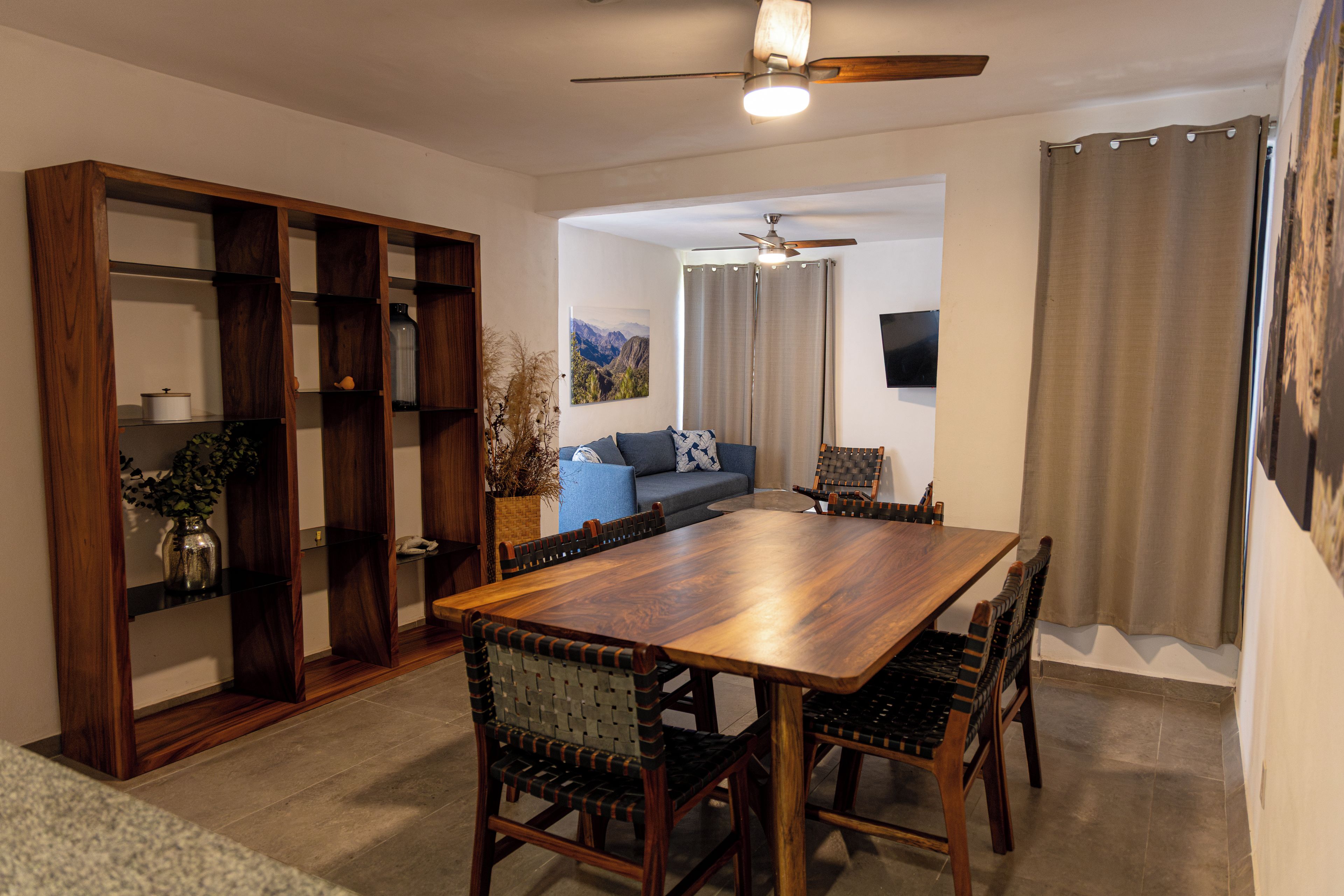 Ein Essbereich mit Holztisch und Stühlen, einem Deckenventilator und Blick auf ein Wohnzimmer mit Sofa und Vorhängen.