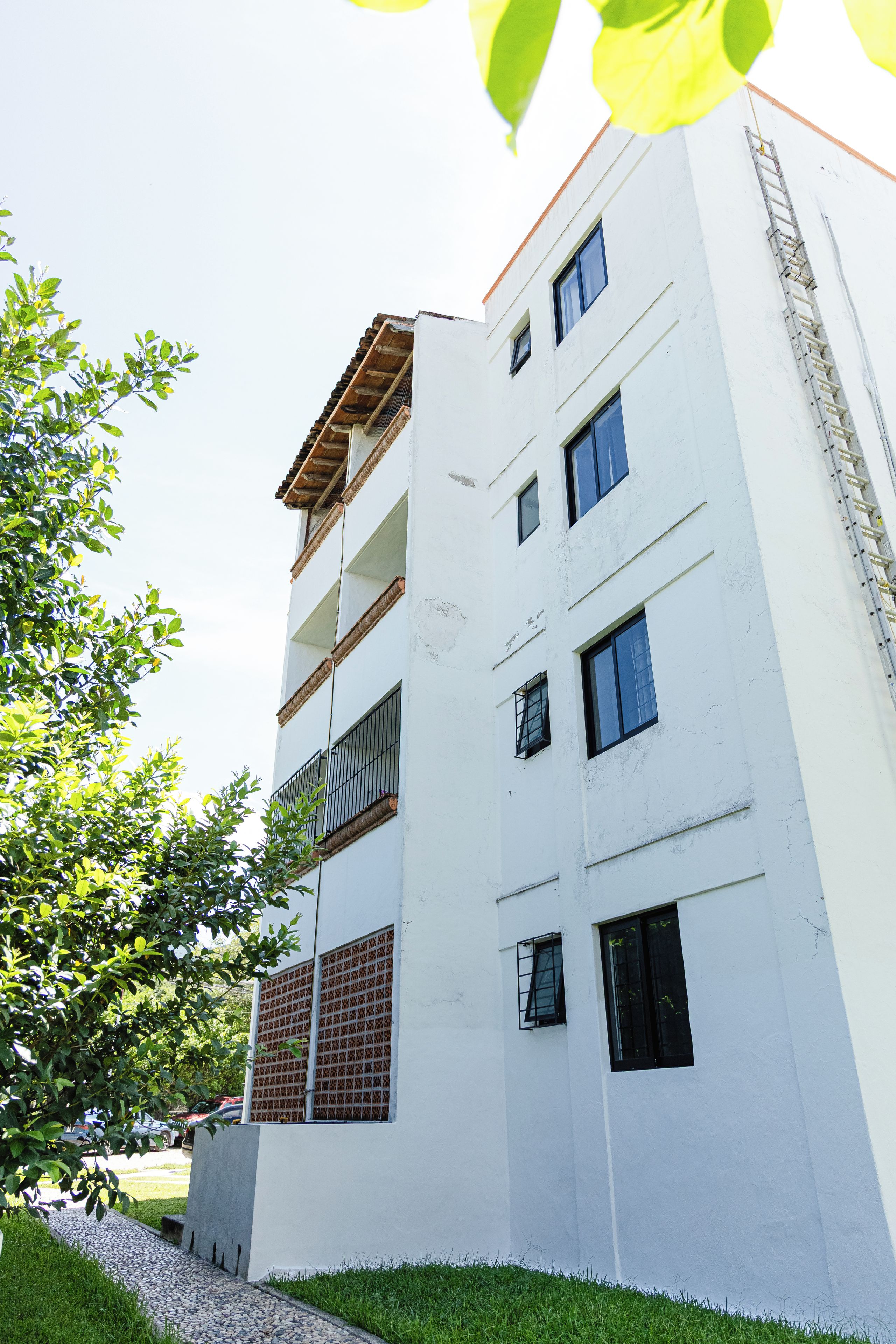 A multi-story building with a white facade, multiple windows, and a visible balcony on the second floor.