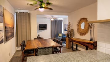 Un comedor con mesa y sillas de madera, ventilador de techo y televisor montado en la pared.