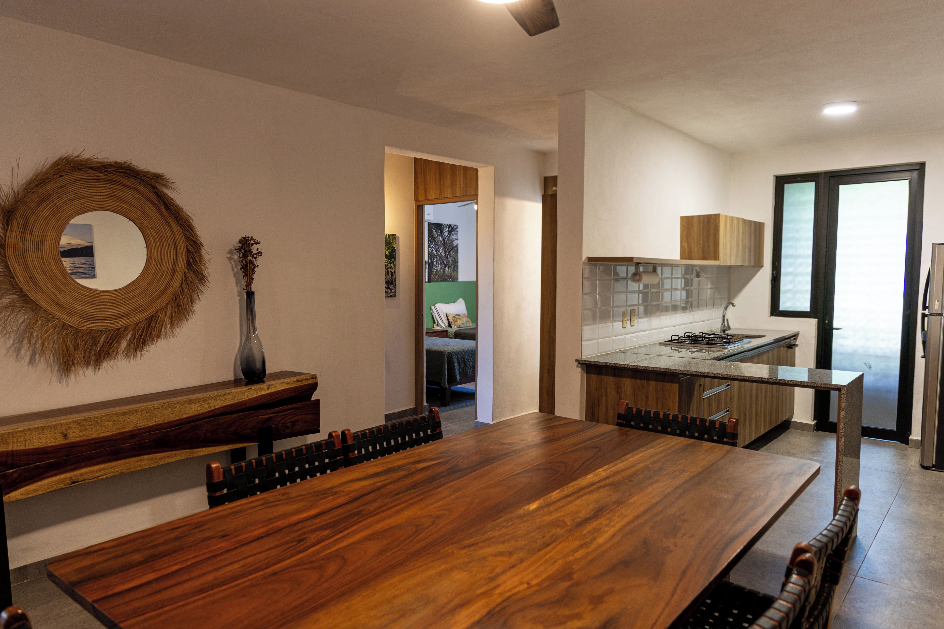 A modern kitchen with a wooden dining table, a built-in stove, and a view of the living area.