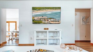 A modern living room with a large window, a white entertainment unit, and a view of a beach and ocean.