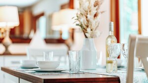 A dining table with a bottle of white wine, two wine glasses, a bowl, and a vase with dried flowers.