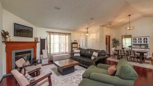 A spacious living room with a fireplace, leather sofa, and a dining area with a kitchen in the background.