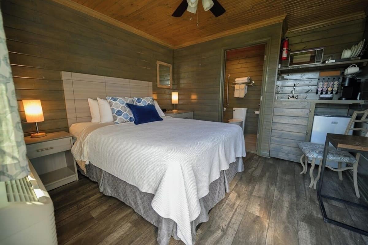 Ein gemütliches Schlafzimmer mit einem großen Bett, Nachttischlampen, einem hölzernen Deckenventilator und einer kleinen Küchenzeile mit Mikrowelle und Kaffeemaschine.
