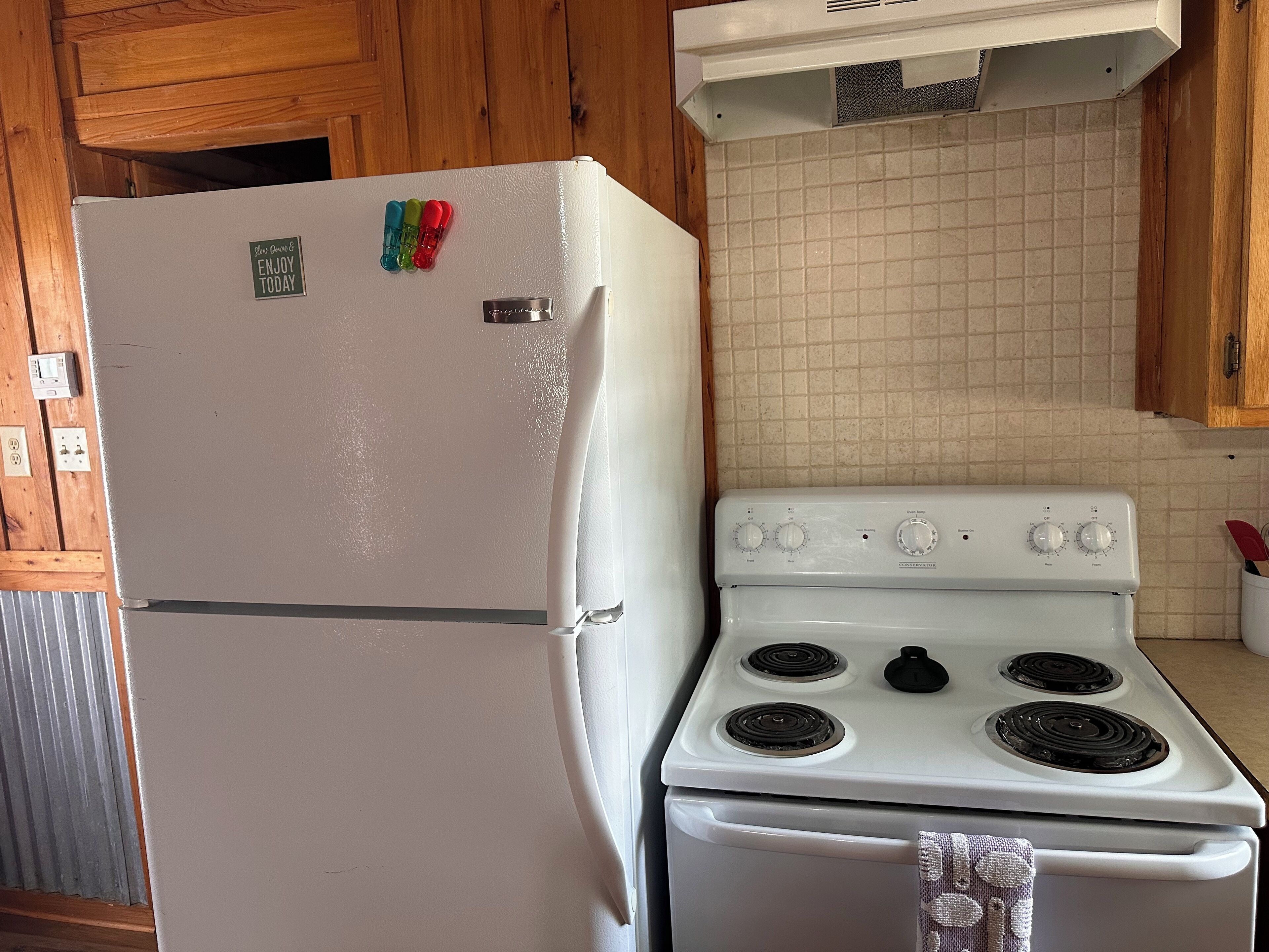 Une cuisine avec un réfrigérateur et une cuisinière blancs, des armoires en bois et un dosseret carrelé.