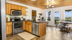 A kitchen with wooden cabinets, stainless steel appliances, and a view through the door. - Mtn View + Pond w/ fishing + Hot Tub + Firepit + EV charger (Ranger)
