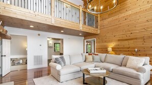 A spacious living area with a large L-shaped sectional sofa, a round coffee table, and a wooden ceiling with a balcony. - Mtn View + Pond w/ fishing + Hot Tub + Firepit + EV charger (Ranger)