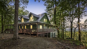 A large, two-story wooden house with a balcony, surrounded by trees. - Mtn View + Pond w/ fishing + Hot Tub + Firepit + EV charger (Ranger)