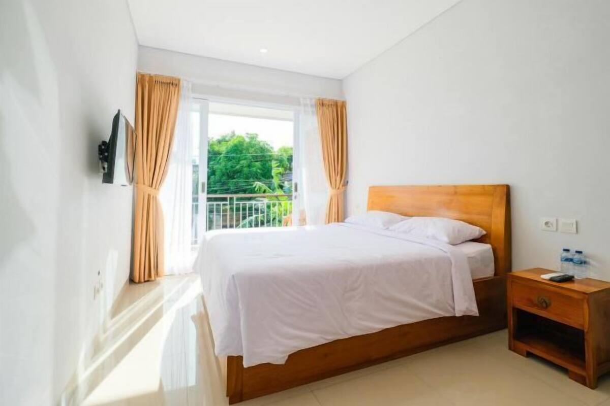 A bedroom with a bed, a nightstand, a TV, and a balcony with curtains.