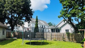 A backyard with a trampoline, a wooden fence, and houses in the background. - Cozy, Private1-bedroom in charming Schenectady with Private Bathroom  (Schenectady)