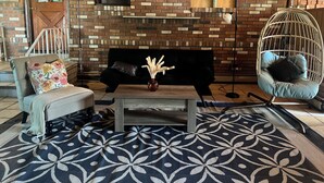 A living room with a brick wall, a sofa, a chair, a hanging chair, a coffee table, and a patterned rug. - Cozy, Private1-bedroom in charming Schenectady with Private Bathroom  (Schenectady)
