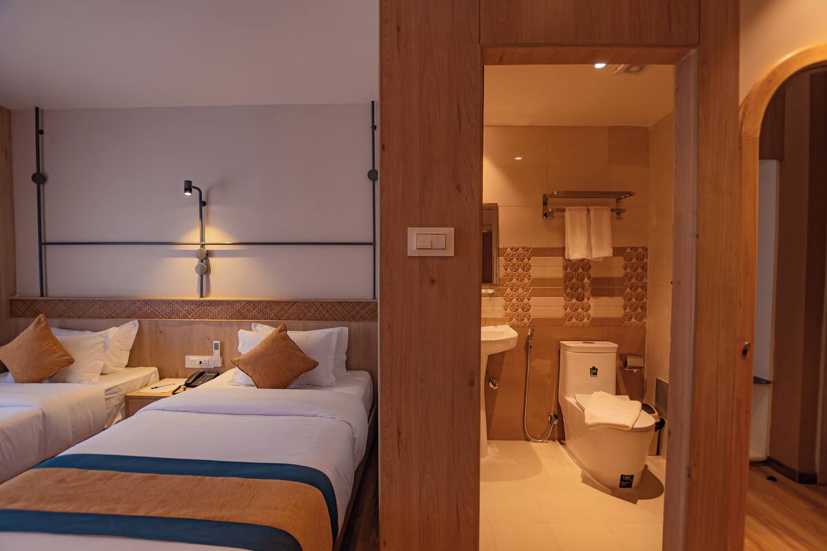 A hotel room with two beds, a bedside table, a lamp, and a view of the bathroom.