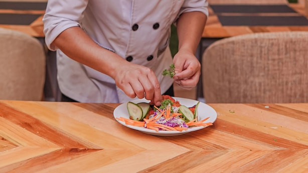 Un chef preparando una ensalada sobre una mesa de madera al aire libre, con una vista panorámica de fondo.