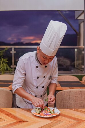 A chef preparing a salad on an outdoor wooden table with a scenic view in the background. - Hotel Vistara (Kathmandu)