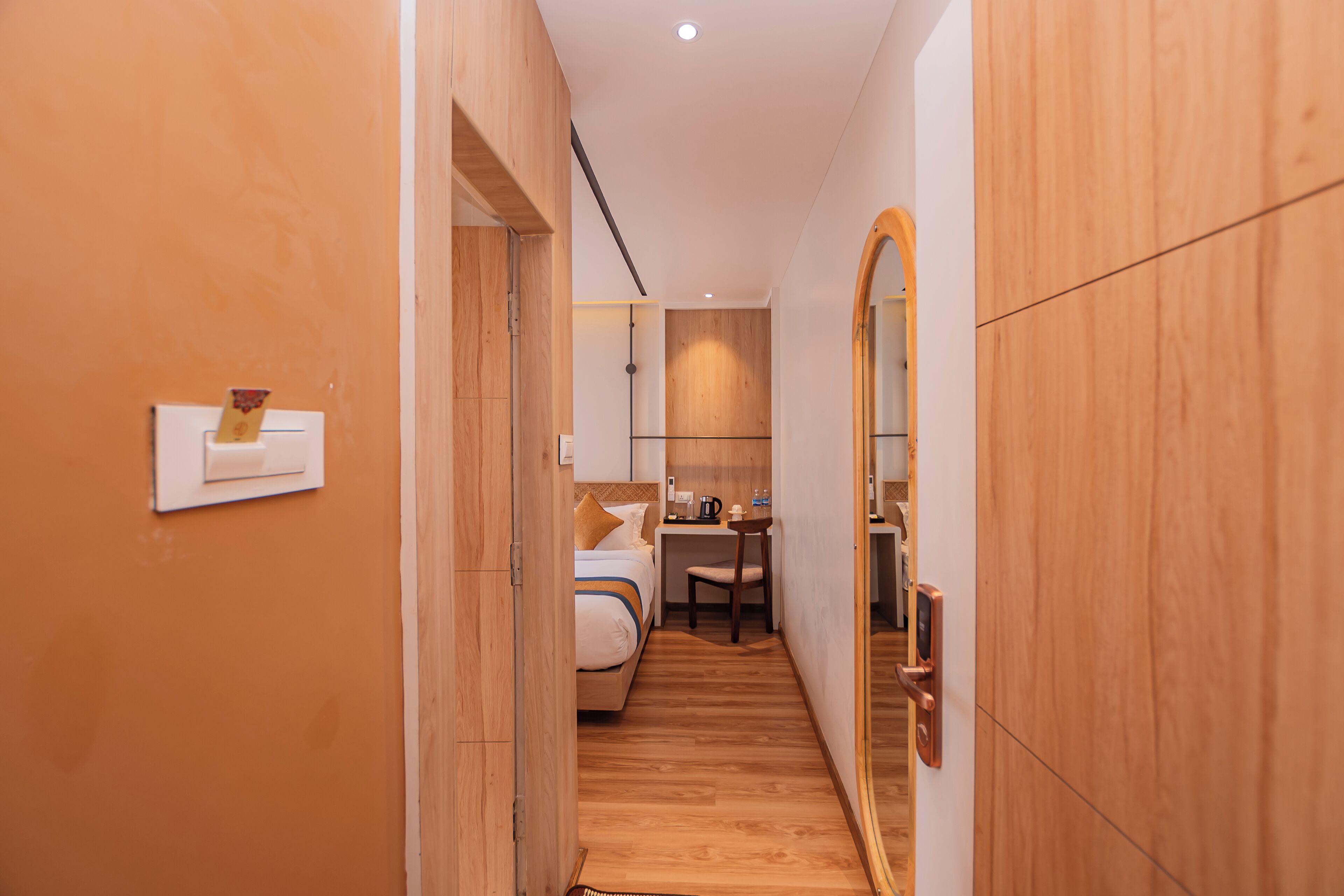 Un couloir étroit avec un lit, un bureau et une chaise, qui mène à une pièce dotée d’un grand miroir et de murs en bois.
