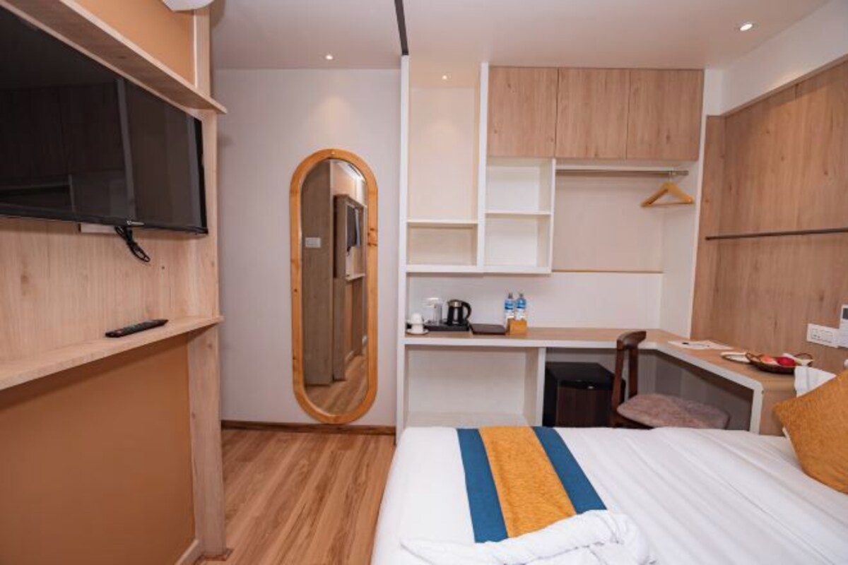 A modern hotel room with a bed, a desk, a mirror, and a TV.