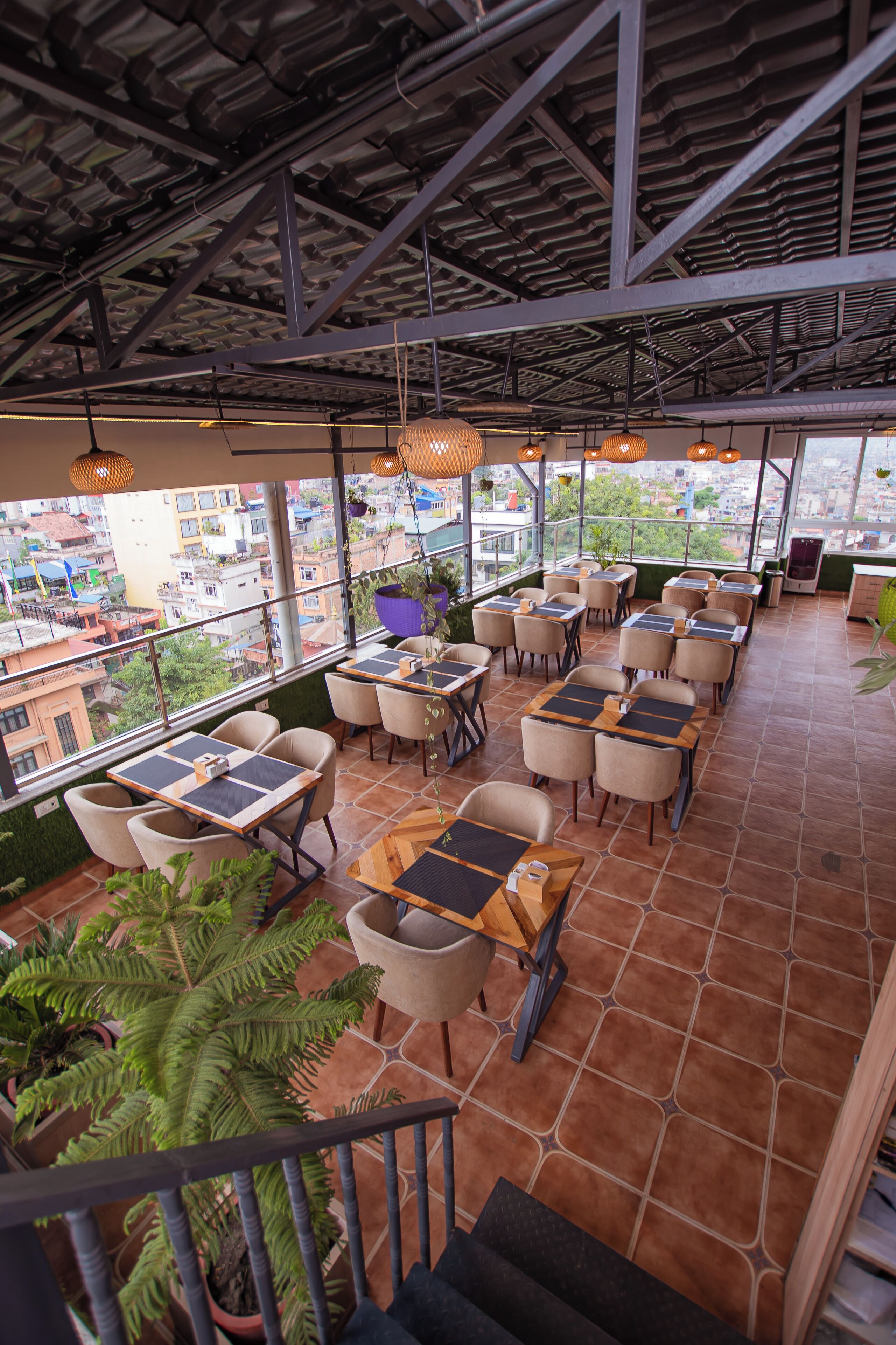 Un restaurante en la azotea con mesas al aire libre, plantas en macetas y vistas de la ciudad.