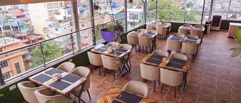 Un restaurante en la azotea con mesas al aire libre, plantas en macetas y vistas de la ciudad.