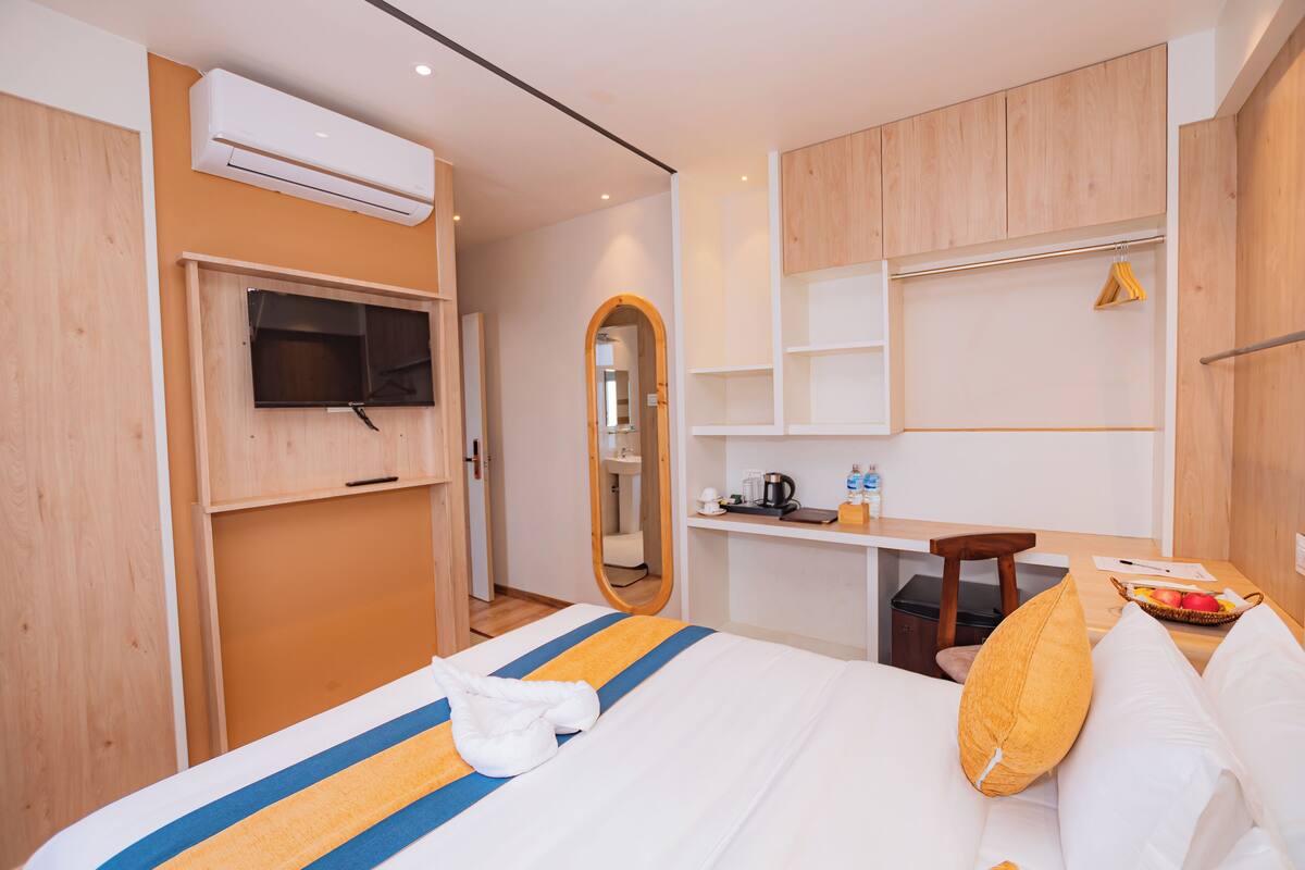 A hotel room with a bed, a desk, a mirror, and a TV.