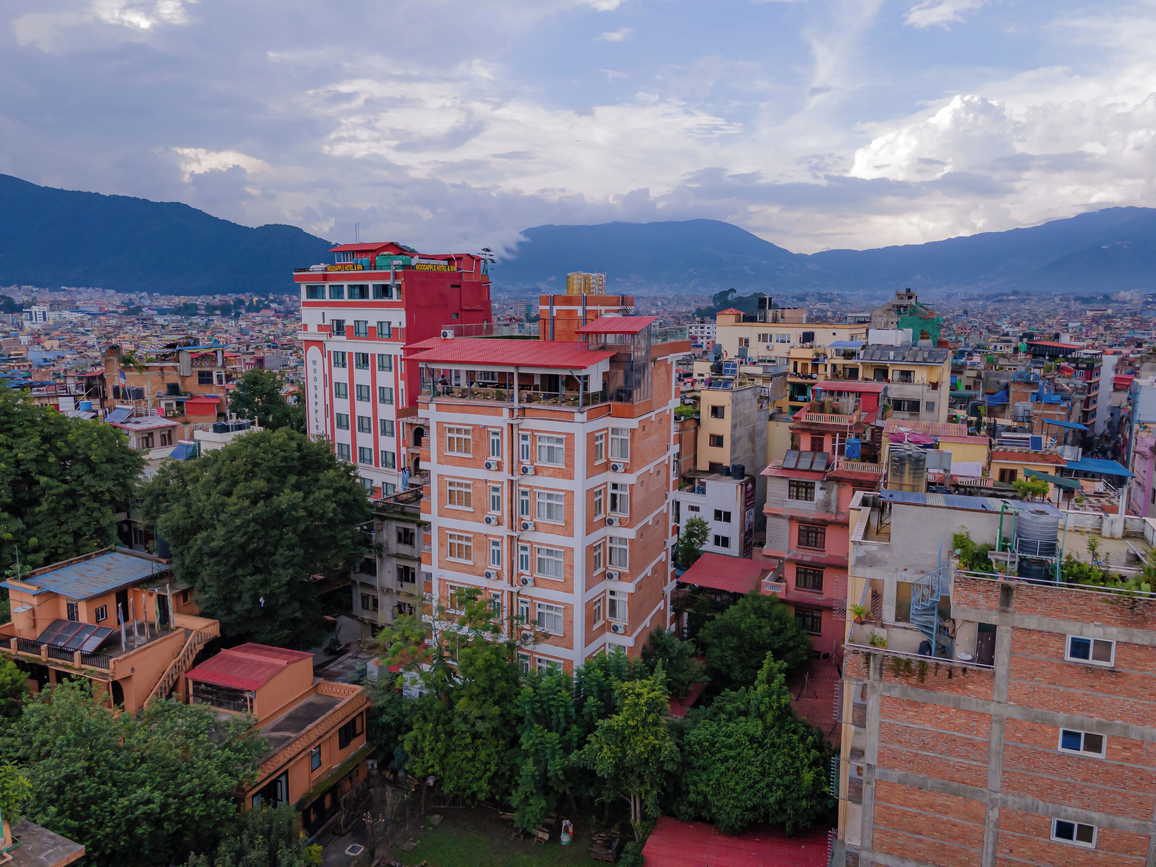 A multi-story hotel with balconies and a view of a cityscape and mountains in the background.
