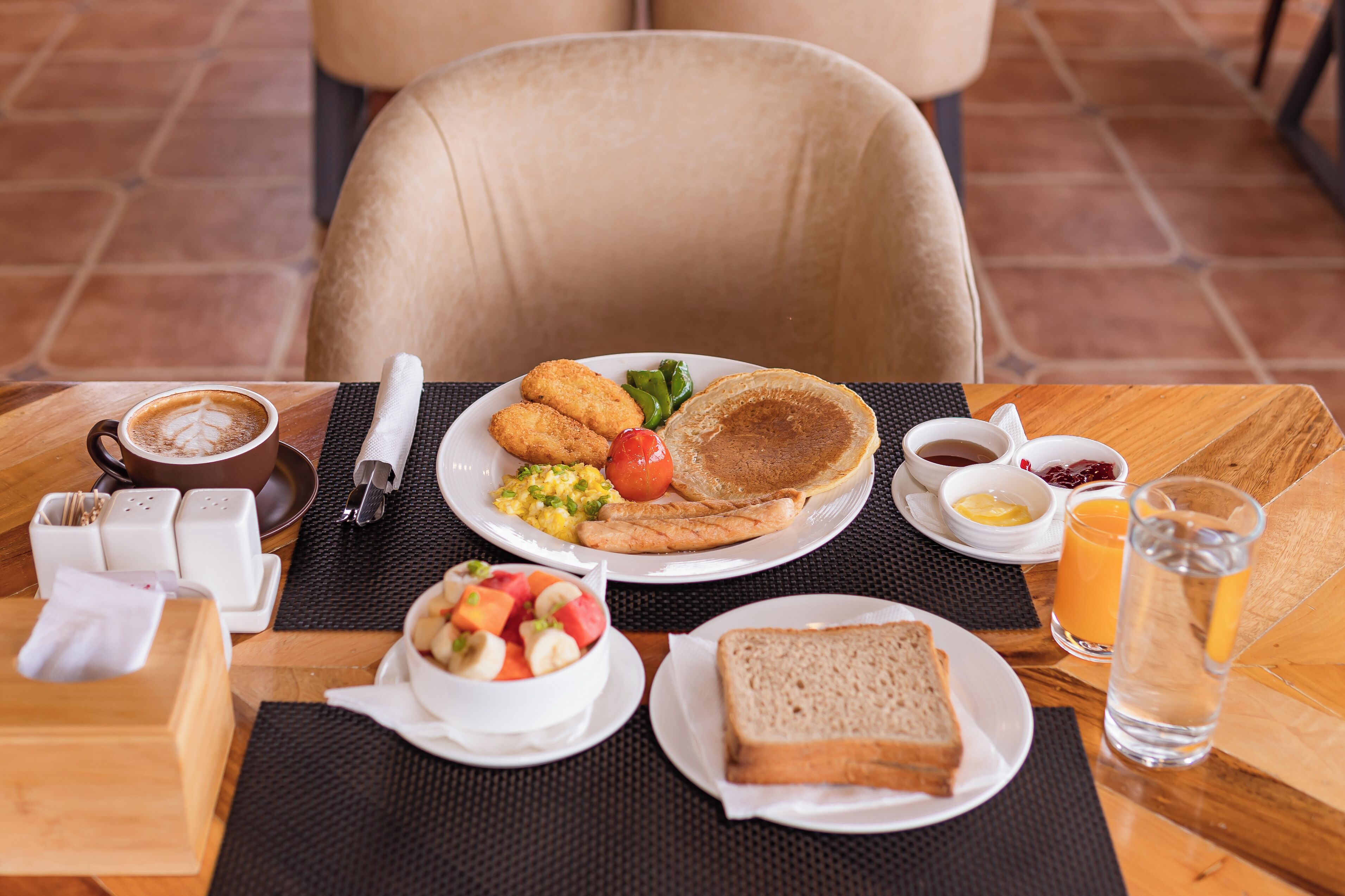 A breakfast table with a plate of eggs, toast, and fruit salad, a cup of coffee, and a glass of orange juice.