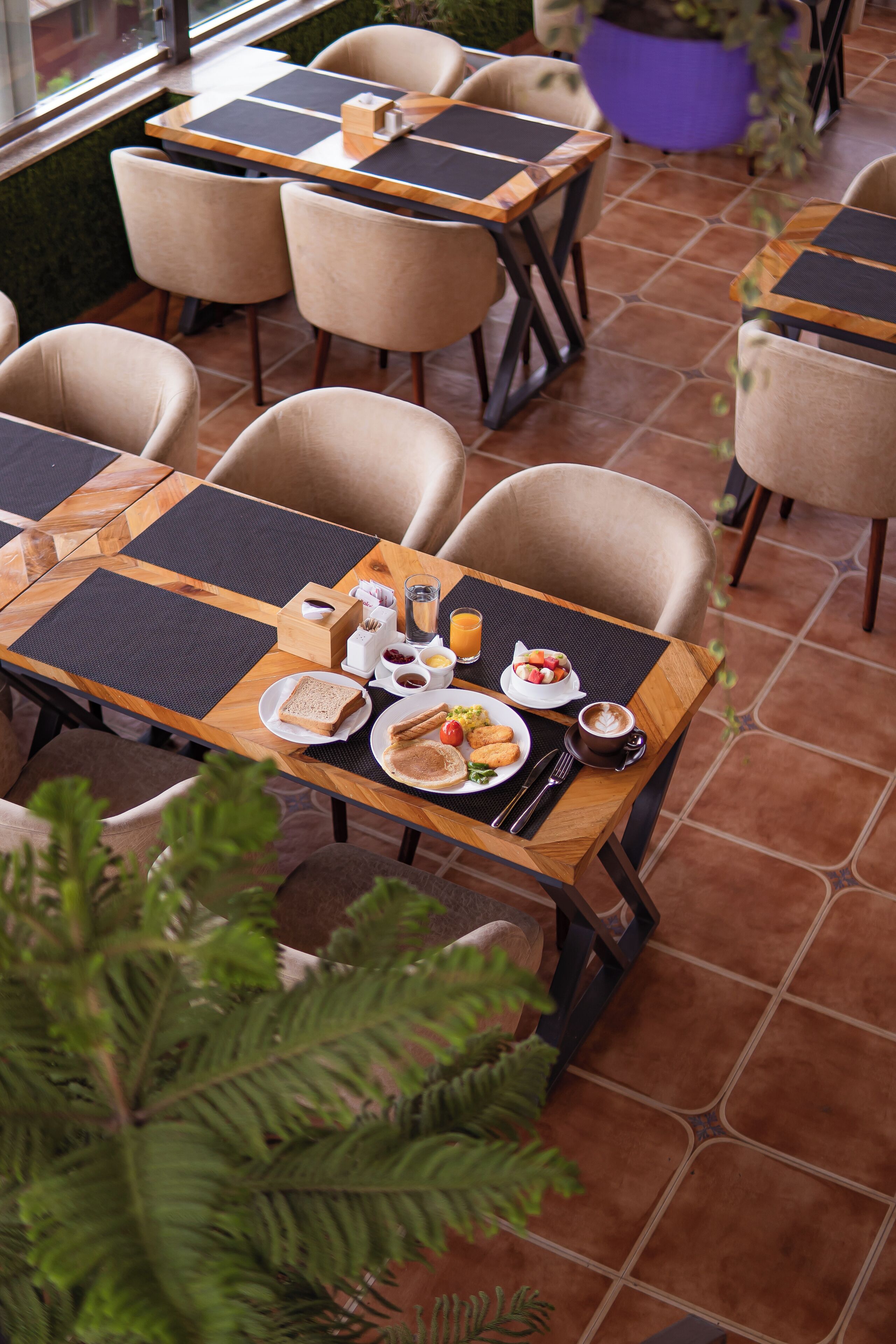 A dining area with multiple tables and chairs, each with a placemat and a set table with plates, cutlery, and a glass of orange juice.