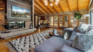 A spacious living room with a fireplace, wooden ceiling beams, a large TV, and a cozy seating area. - The Lodge at Wildwood (South Lake Tahoe)