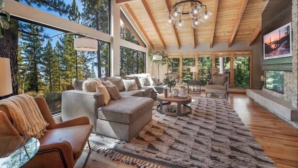 A spacious living room with a large window, wooden ceiling beams, and a cozy fireplace. - The Lodge at Wildwood (South Lake Tahoe)