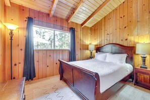 A wooden-paneled bedroom with a large bed, two bedside lamps, and a window with curtains.