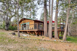 A wooden cabin with a deck, surrounded by trees.