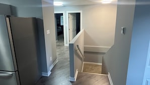 Un pasillo con un refrigerador, una escalera y una puerta que da a otra habitación.