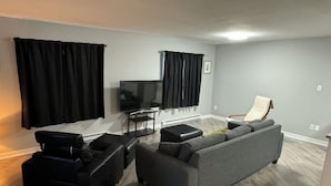 Una sala de estar moderna con un sofá gris, sillones de cuero negro, un televisor de pantalla plana y cortinas negras.