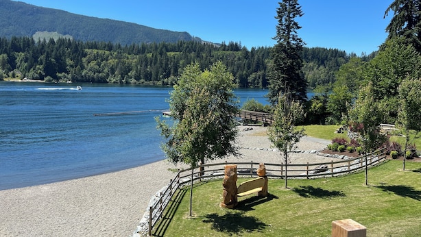 Vista al lago con un banco de madera y esculturas de osos, rodeado de árboles y una valla de madera.