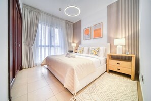 A modern bedroom with a large bed, bedside lamps, a wooden nightstand, and a view of the outdoors.