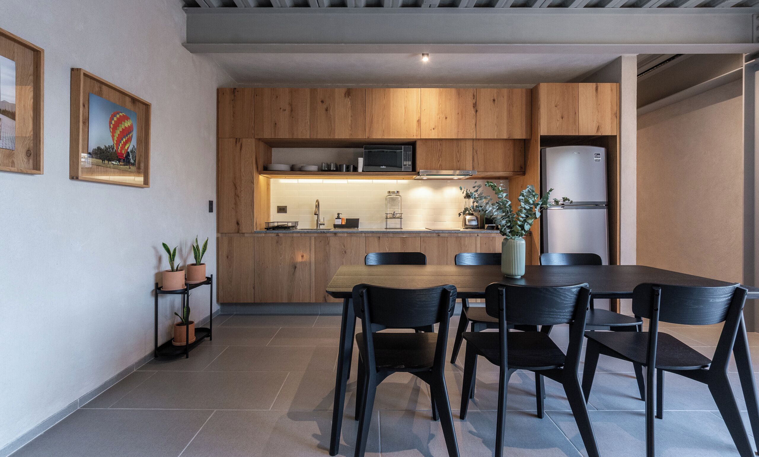 Una cucina moderna con mobili in legno, un forno a microonde e un frigorifero. C'è un tavolo da pranzo con sedie e piante in vaso.