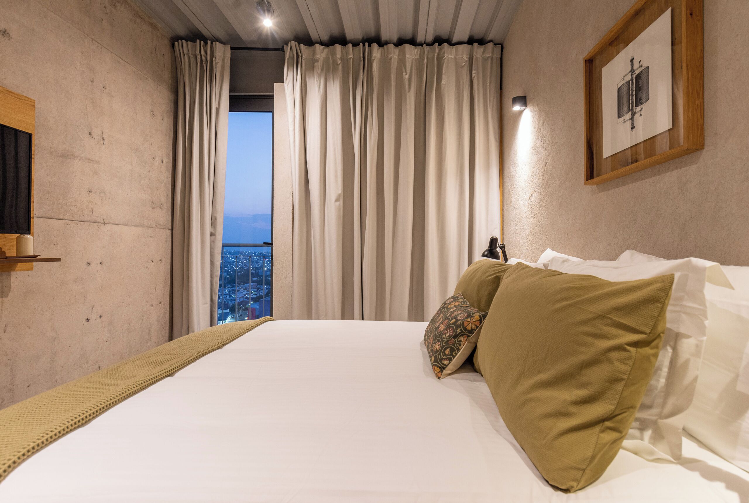 A bedroom with a large bed, a view through the window, and a framed picture on the wall.