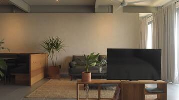 A modern living room with a flat-screen TV, wooden furniture, potted plants, and a ceiling fan.