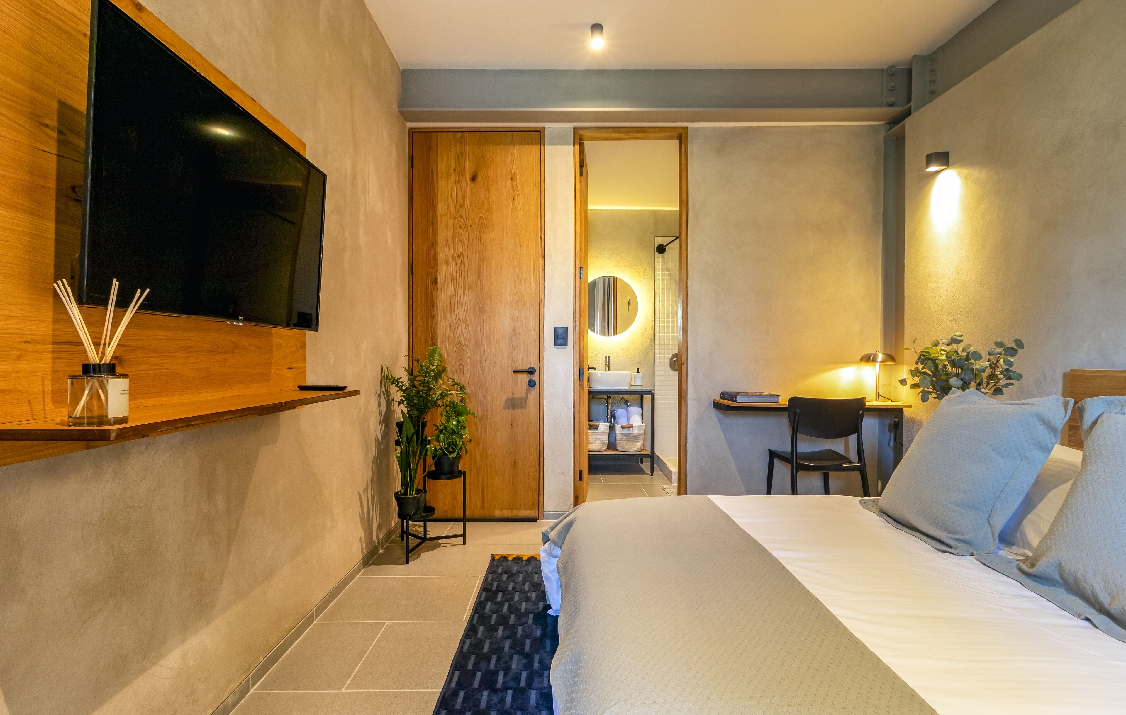 Een moderne hotelkamer met een groot bed, een bureau met stoel, een aan de muur bevestigde televisie en een badkamer die door een geopende deur zichtbaar is.