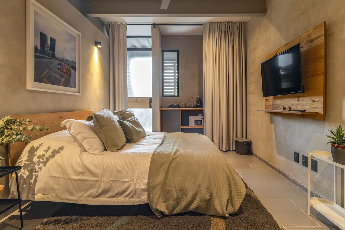 Un dormitorio moderno con una cama grande, un televisor montado en la pared y vistas a la ciudad desde la ventana.