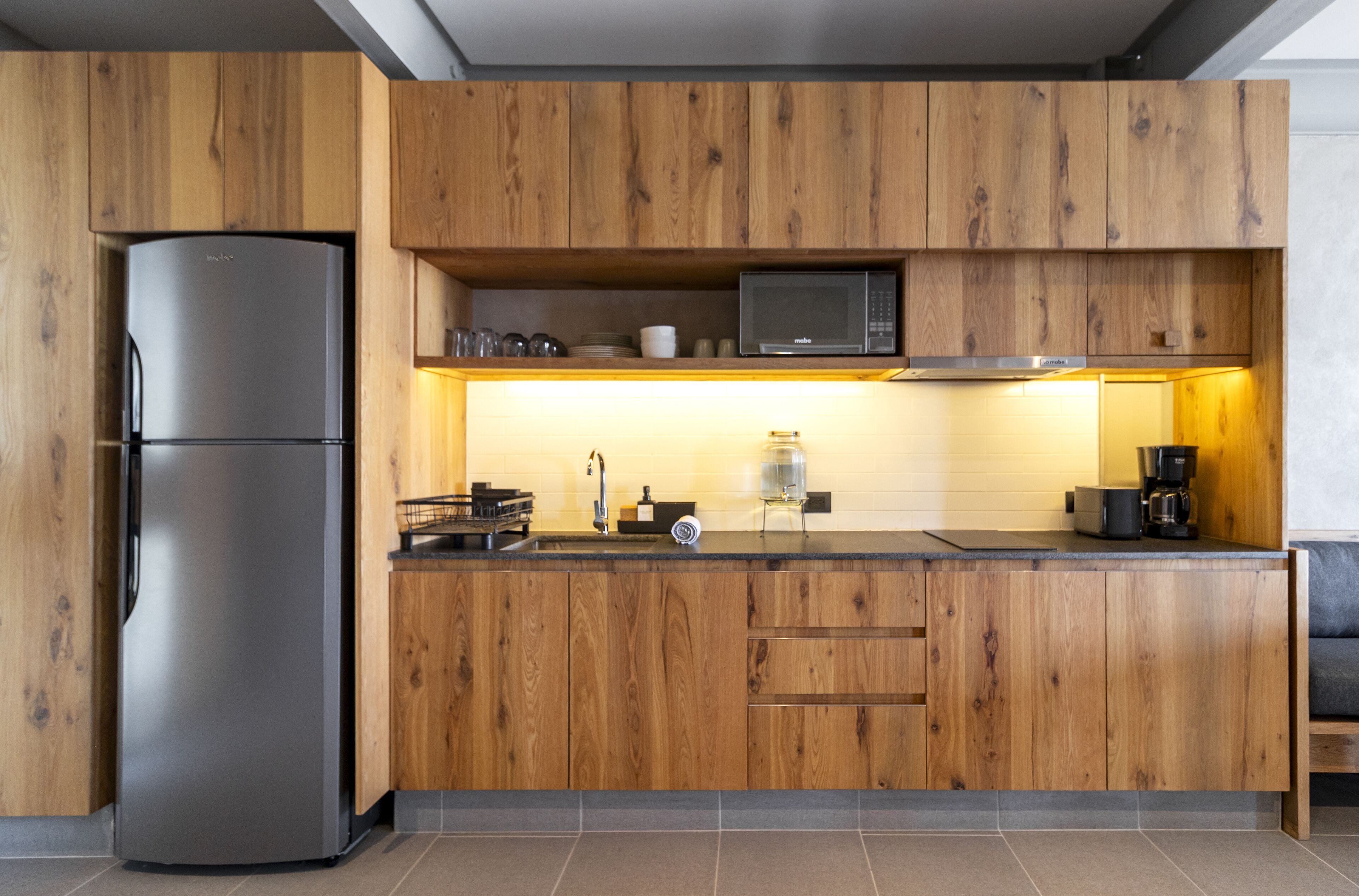 Une cuisine moderne avec des meubles en bois, un réfrigérateur en acier inoxydable, un four à micro-ondes et une machine à café.