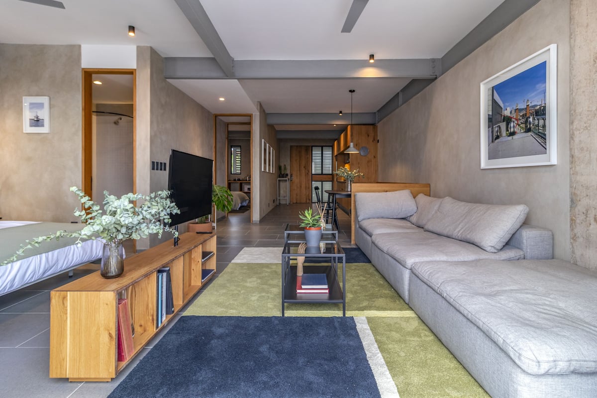 Una sala de estar moderna con sofá, televisor, estantería y una zona de comedor al fondo.