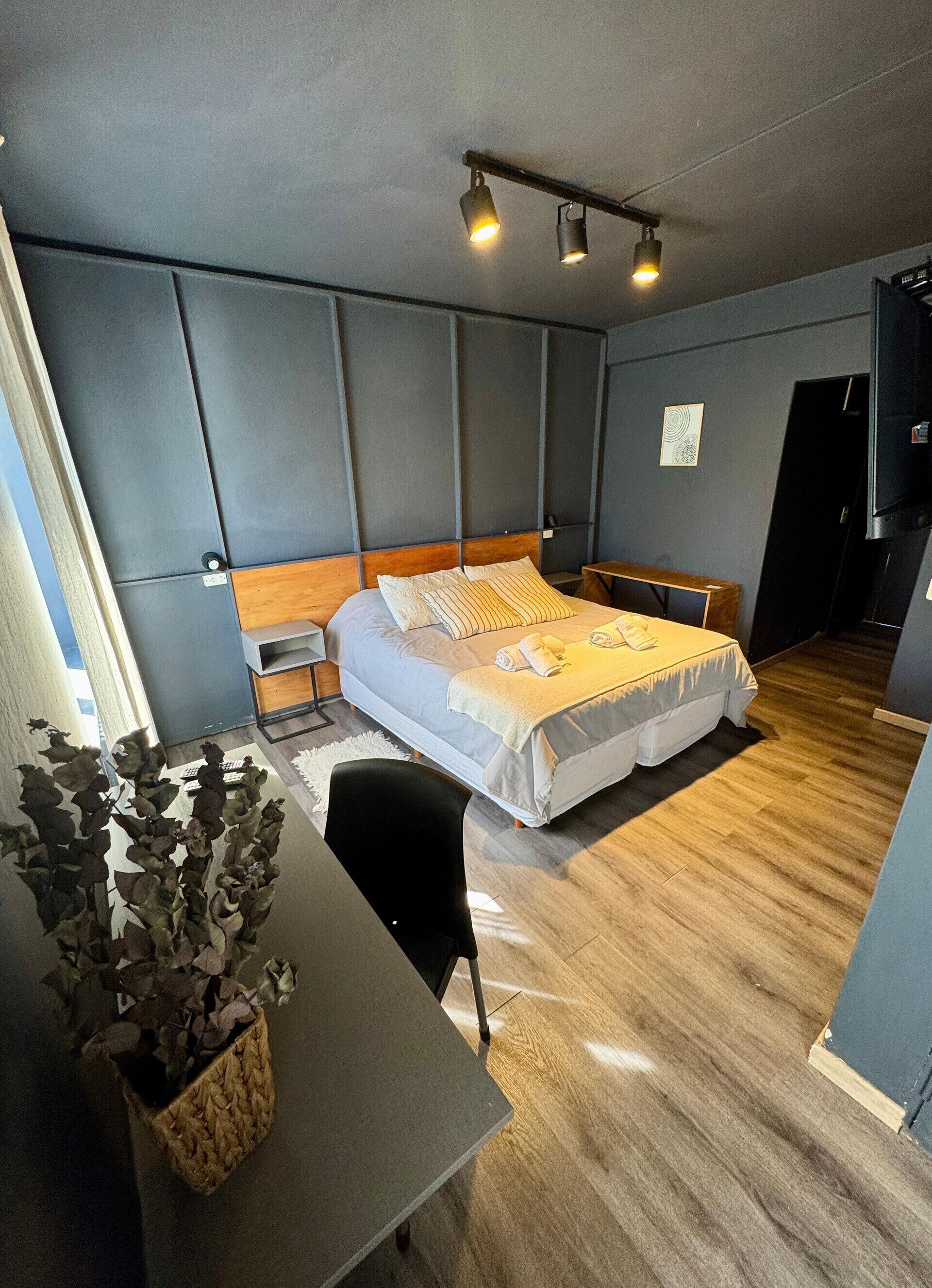 Un dormitorio moderno con una cama grande, mesitas de noche, un escritorio y una planta en maceta.