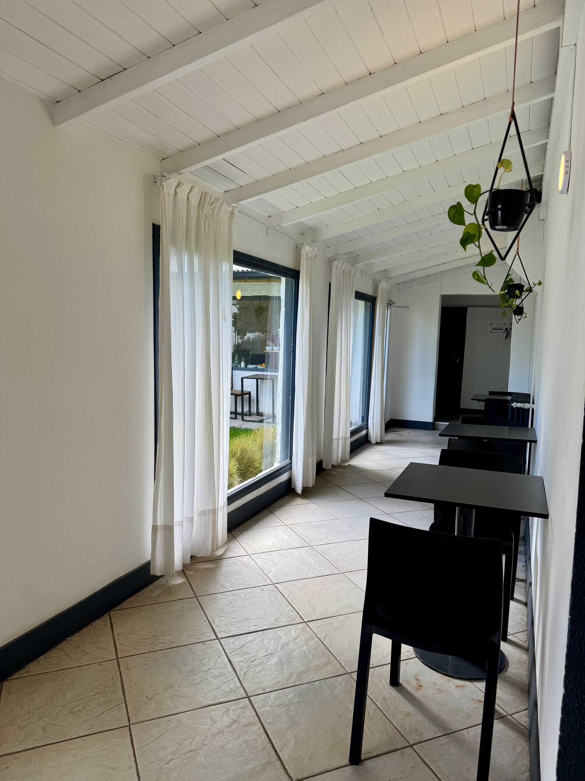 A spacious room with a high ceiling, large windows with white curtains, and a tiled floor.