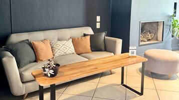 Una sala de estar moderna con un sofá, una mesa de centro de madera y un reposapiés redondo pequeño. Hay tres obras de arte colgadas en la pared sobre el sofá.