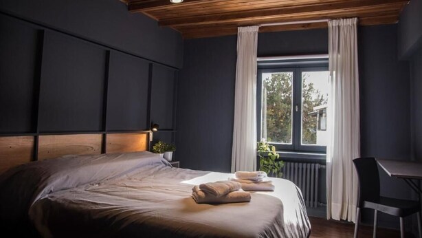 A modern bedroom with a large bed, a desk, and a window with curtains. - Luma Boutique Hotel (San Carlos de Bariloche)