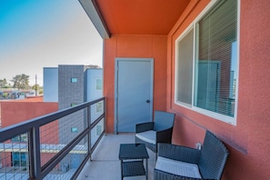 A balcony with a door, two wicker chairs, a small table, and a window with blinds.