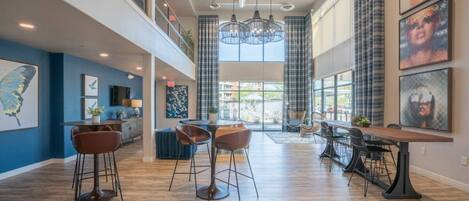 A spacious hotel lobby with a high ceiling, modern lighting fixtures, and a central seating area with bar stools.