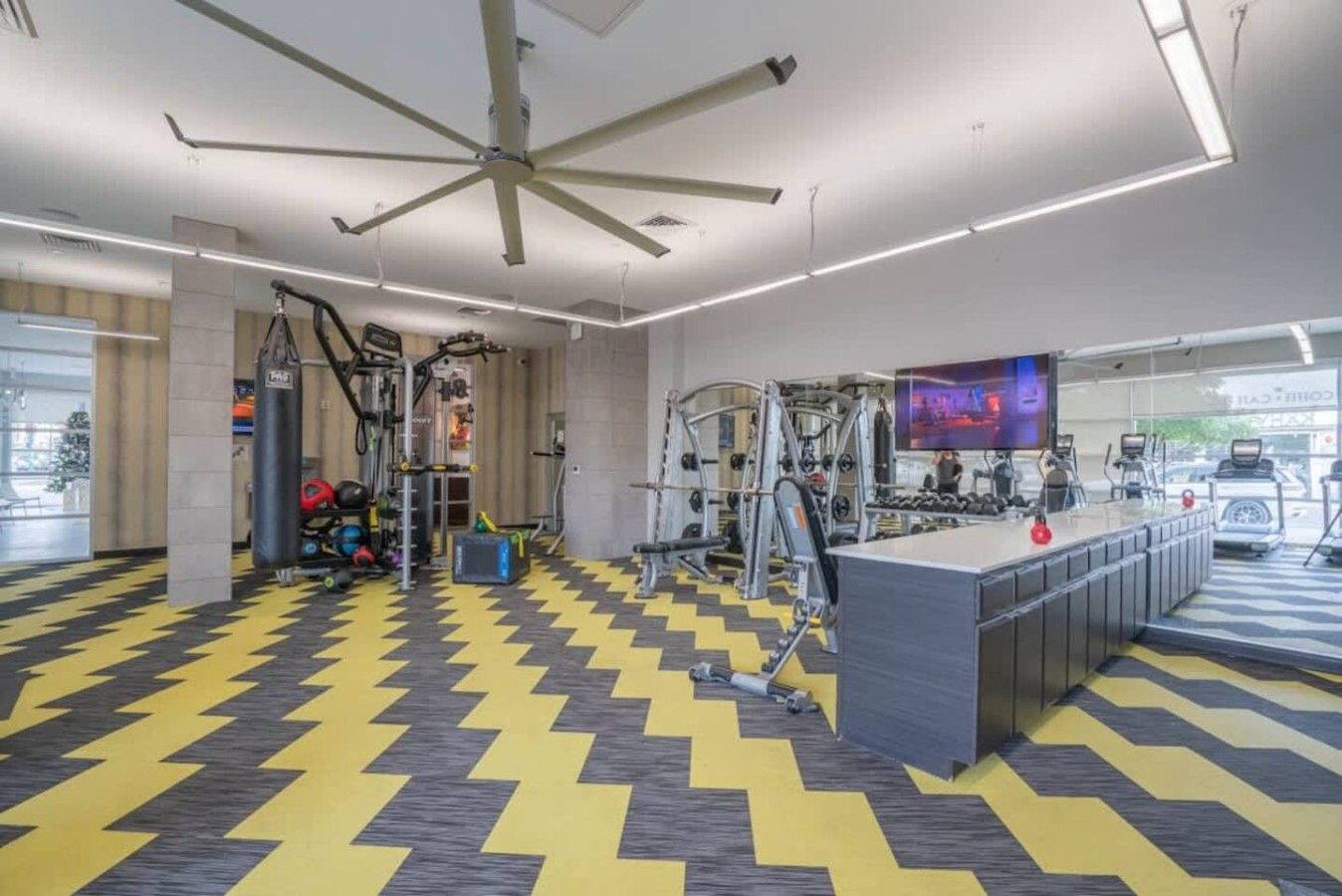 Un gimnasio con equipo de ejercicio, un ventilador de techo y una pantalla de televisión.